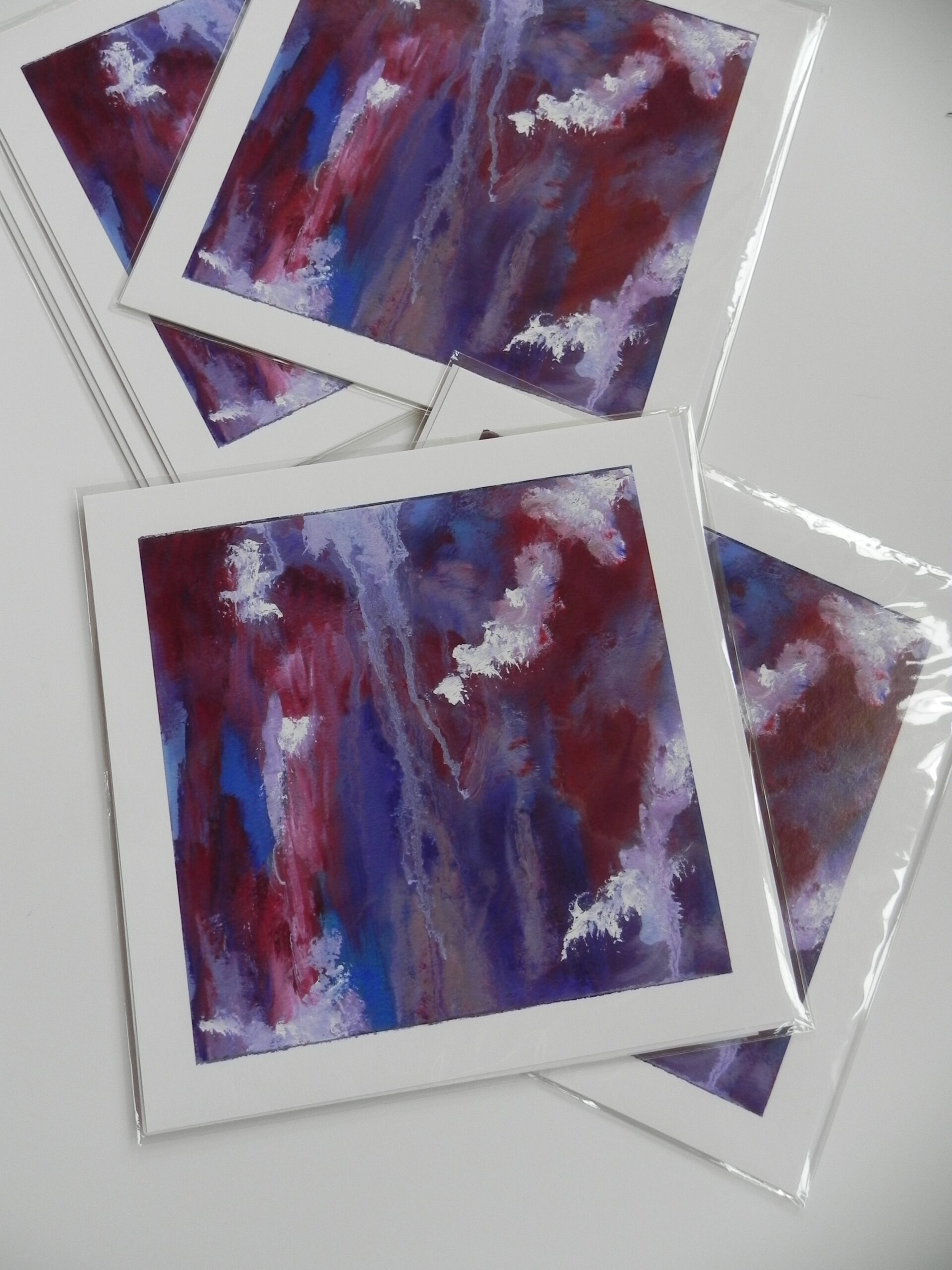 Stack of abstract art prints with red, blue, and white vertical brushstrokes in clear plastic sleeves