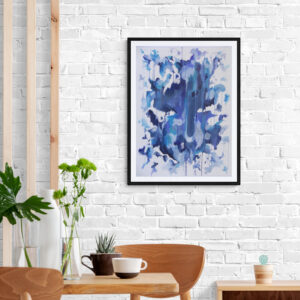 Abstract blue artwork in a black frame hanging above a wooden dining table with plants on a white brick wall.