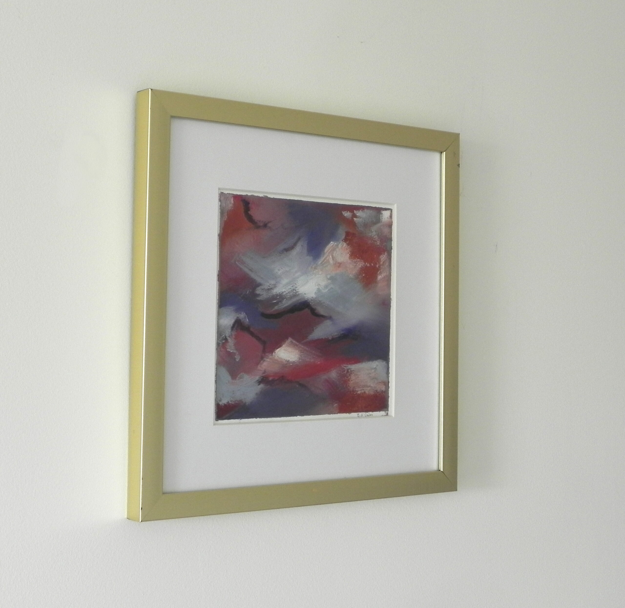 Framed abstract art print with red, blue, and white hues in a gold frame