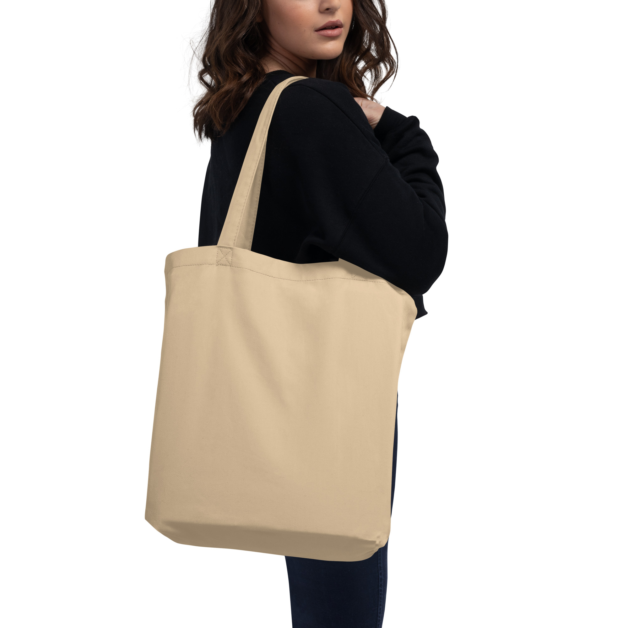 Beige canvas tote bag carried on shoulder by woman in black sweater