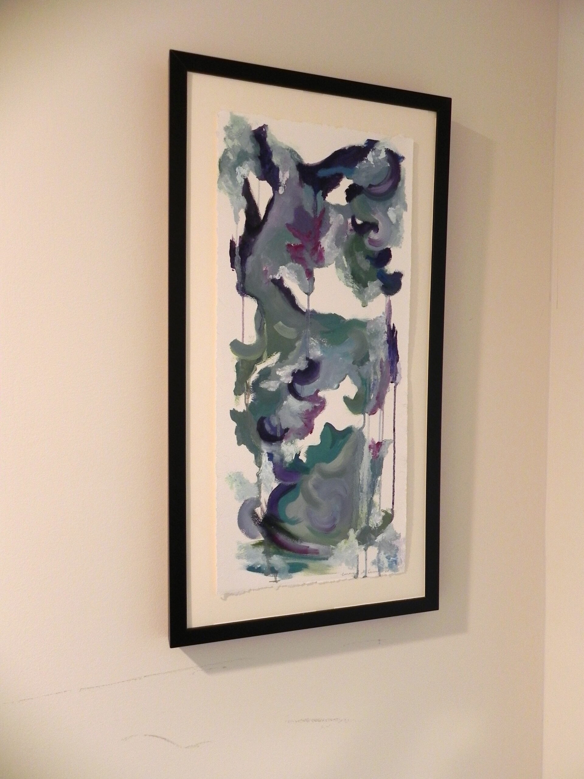 Framed abstract watercolor painting with blue, green, and purple hues on a white wall