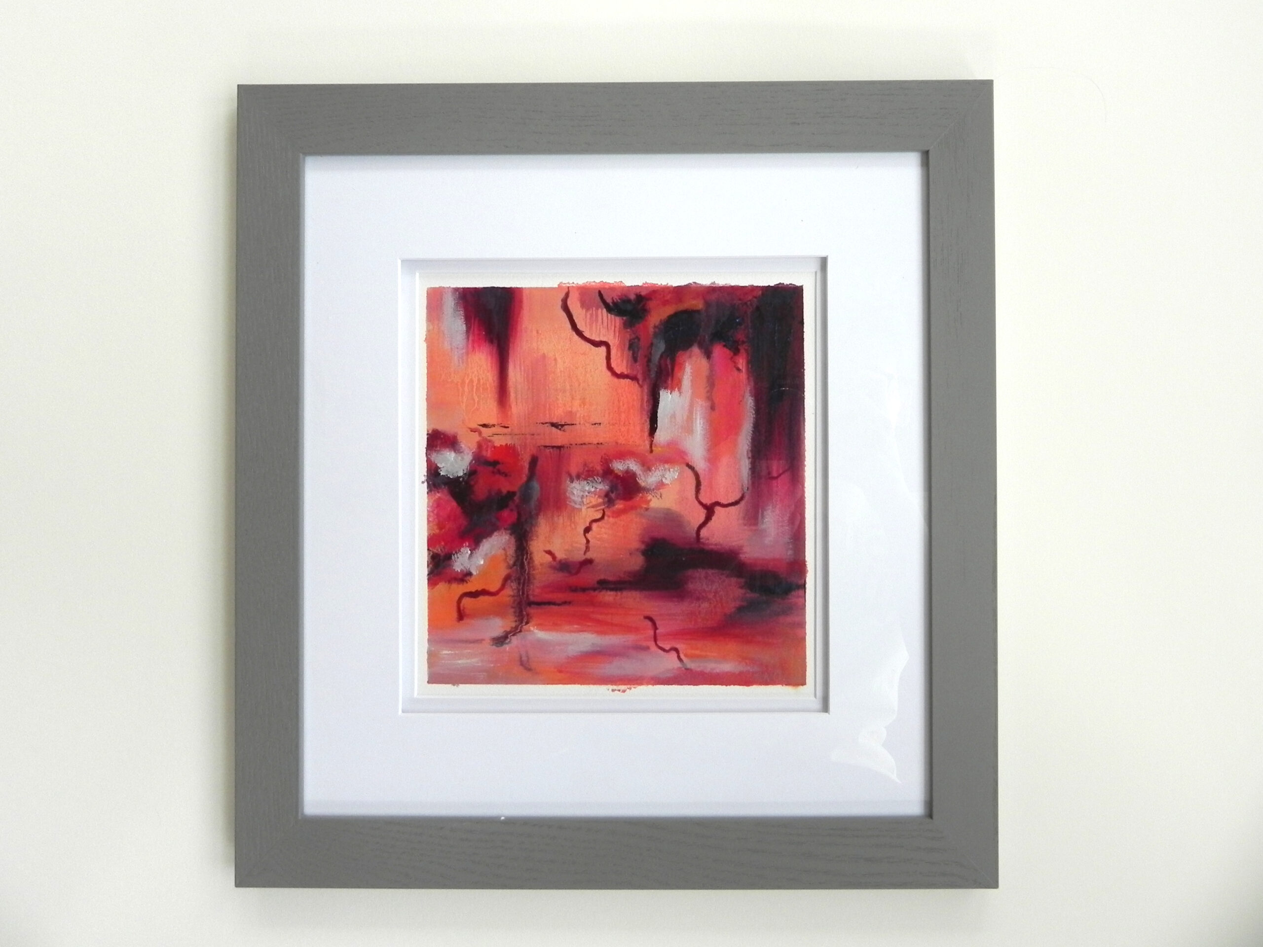 Framed abstract art print with red and orange hues in grey frame