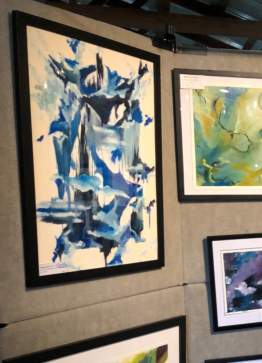 Framed abstract watercolor painting with blue and black brushstrokes on gallery wall