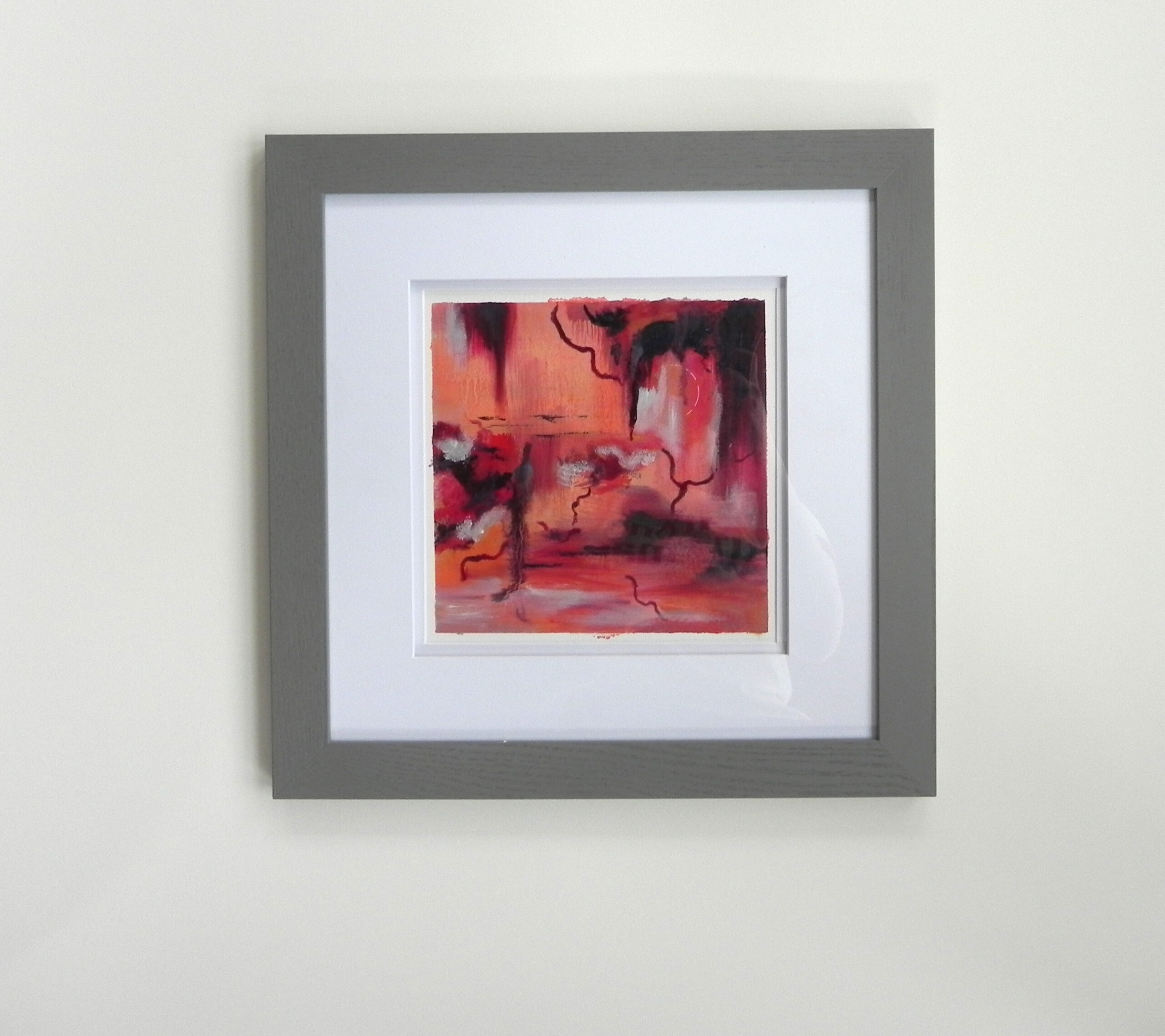 Framed abstract art print with red and orange tones in a grey frame