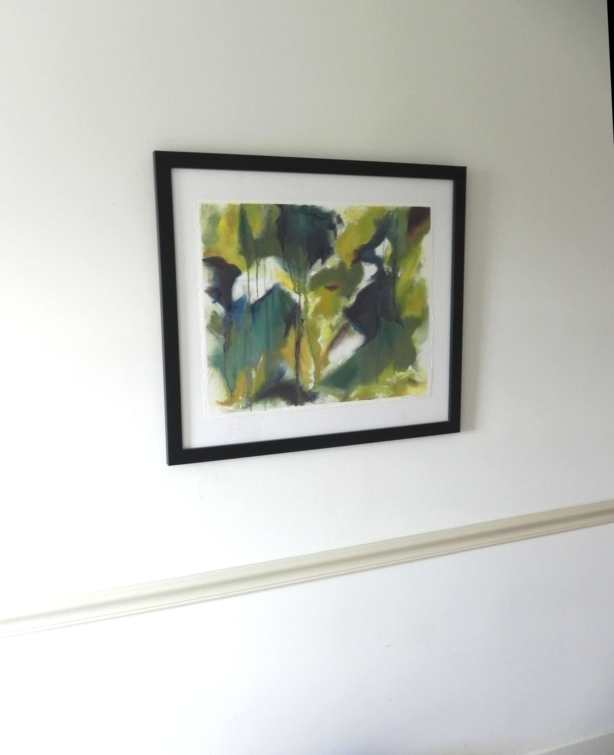 Framed abstract watercolor print with green and yellow hues in black frame