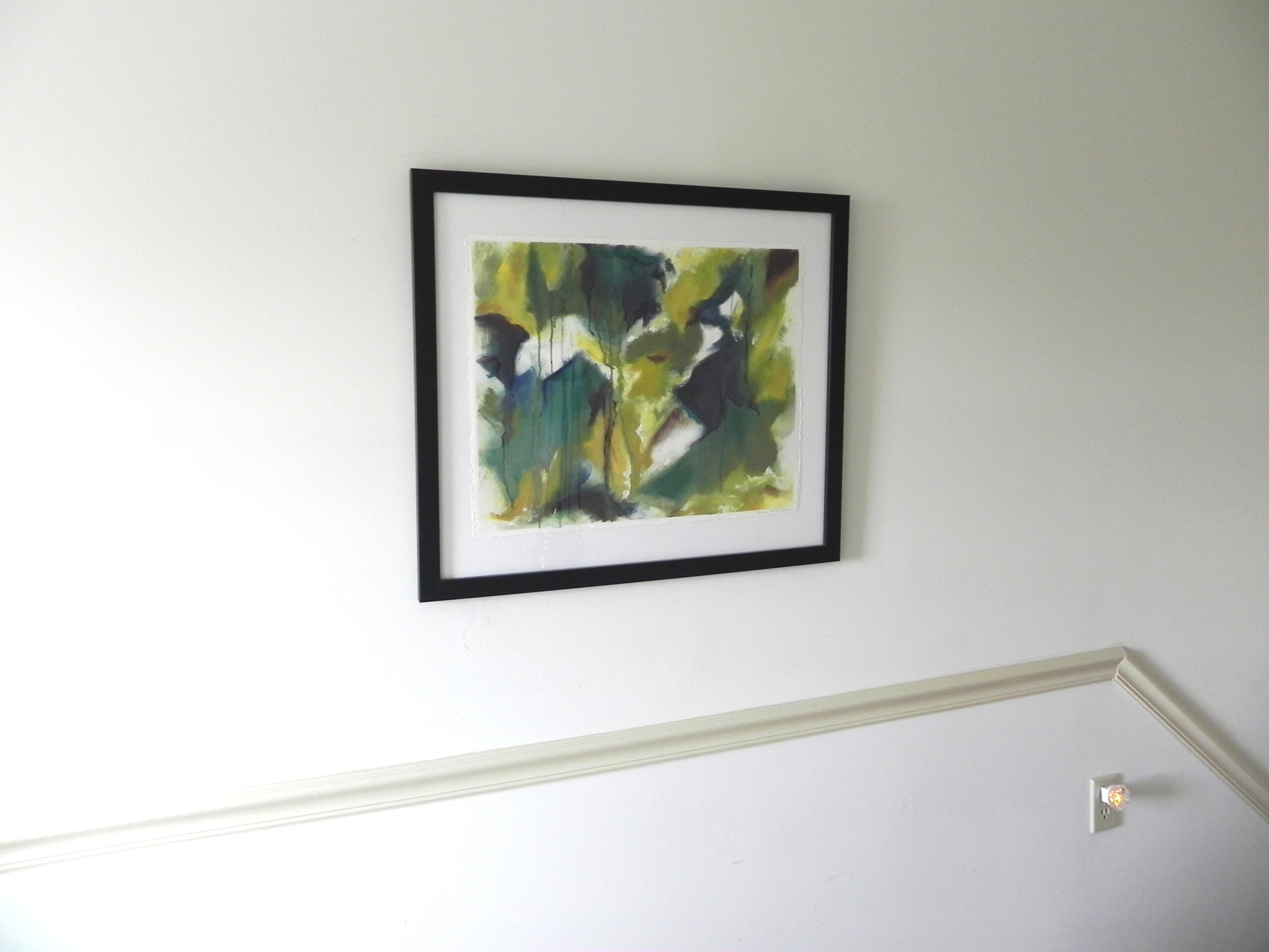 Framed abstract watercolor print with green and blue hues on white wall