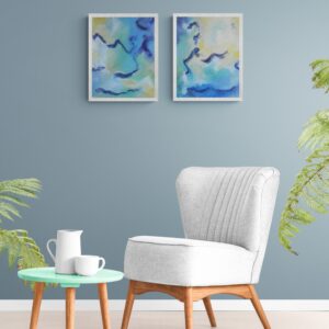 Abstract blue and green diptych artwork in white frames hanging above a white armchair with plants nearby.
