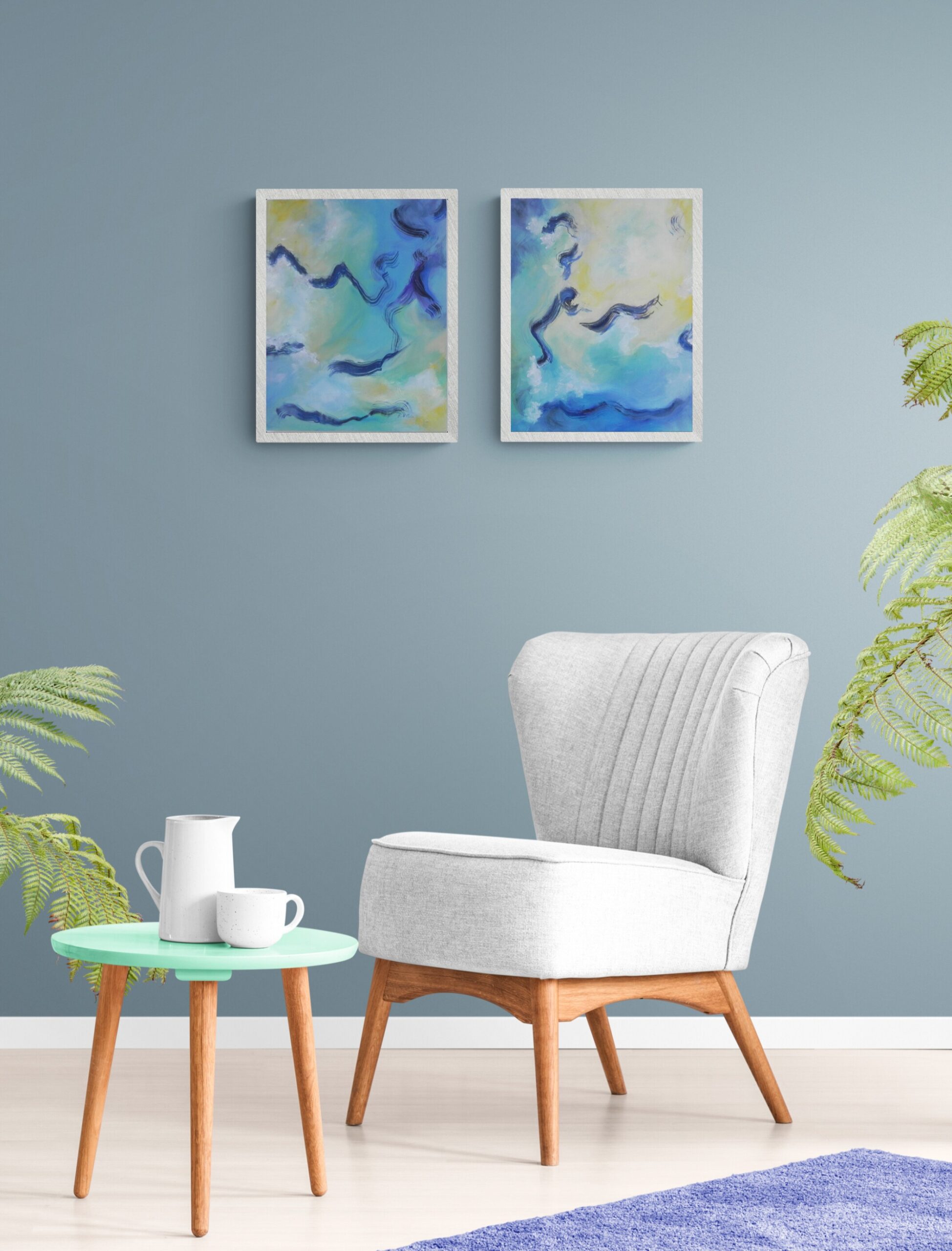 Abstract blue and green diptych artwork in white frames hanging above a white armchair with plants nearby.