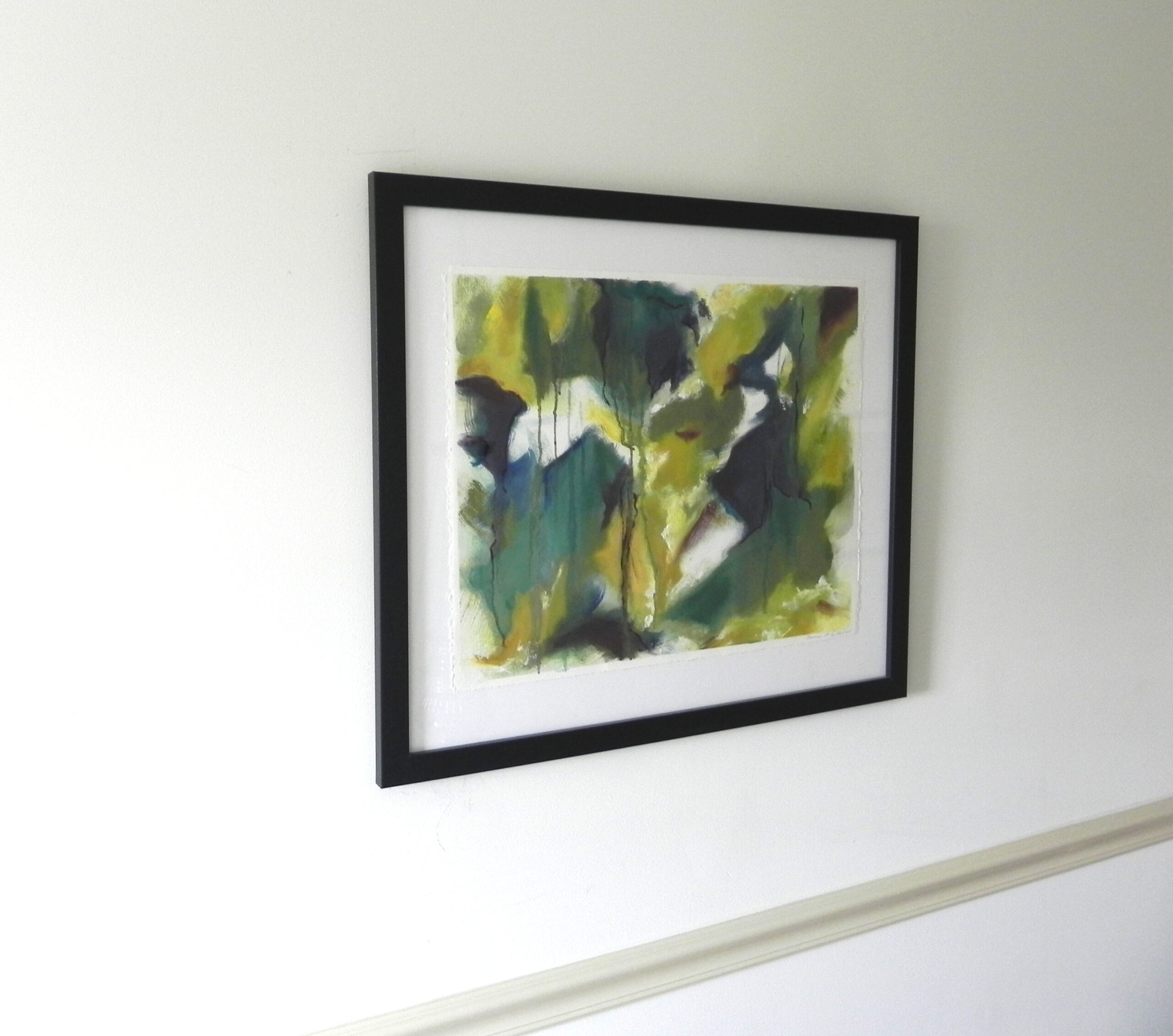 Framed abstract watercolor print with green and yellow hues on white wall