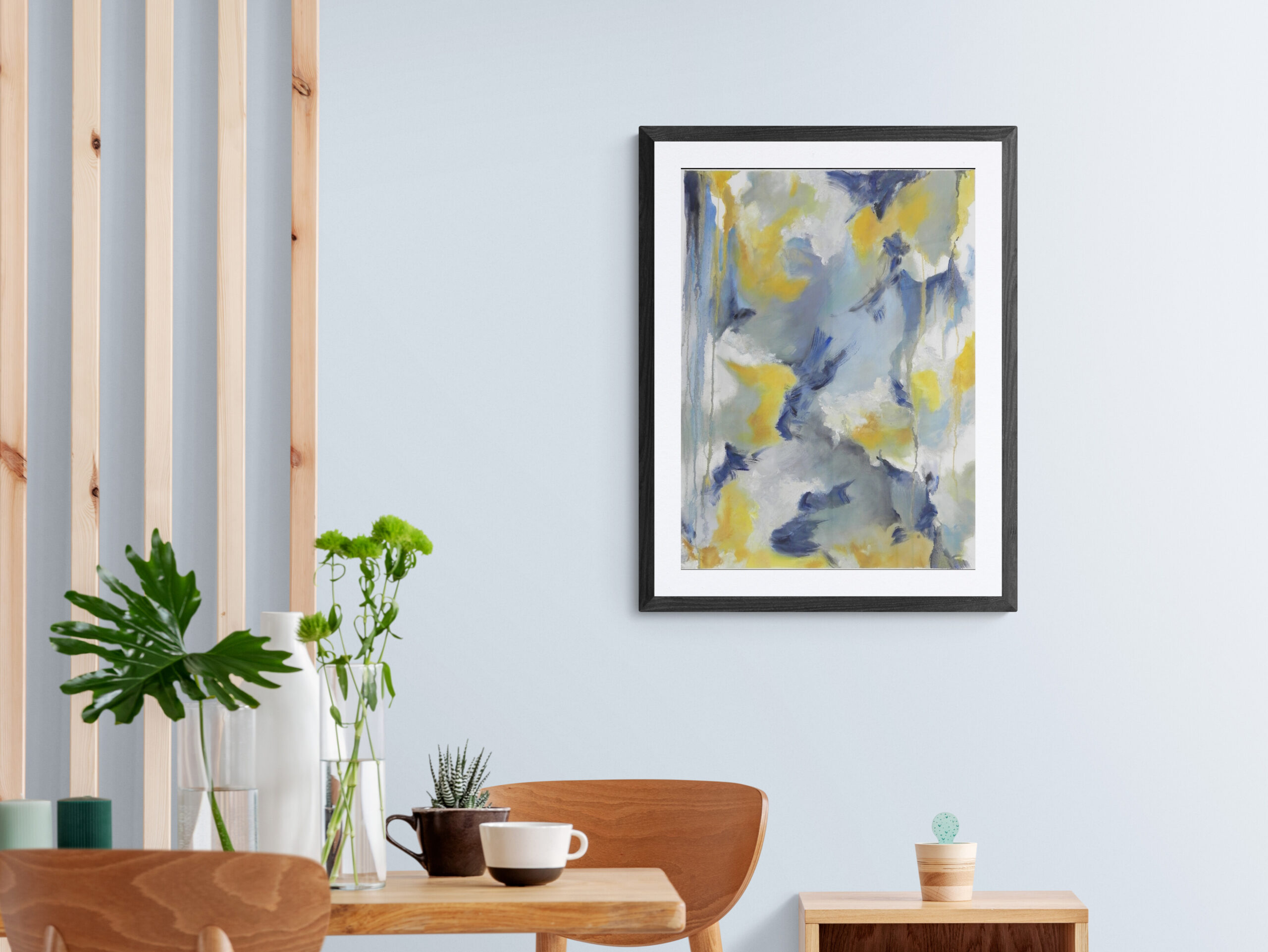 Framed abstract art print with blue, yellow, and white brushstrokes hanging on light blue wall