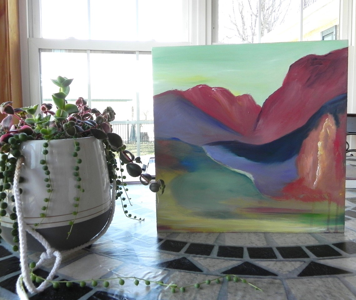 Abstract landscape painting with red mountains and blue river displayed on tiled table