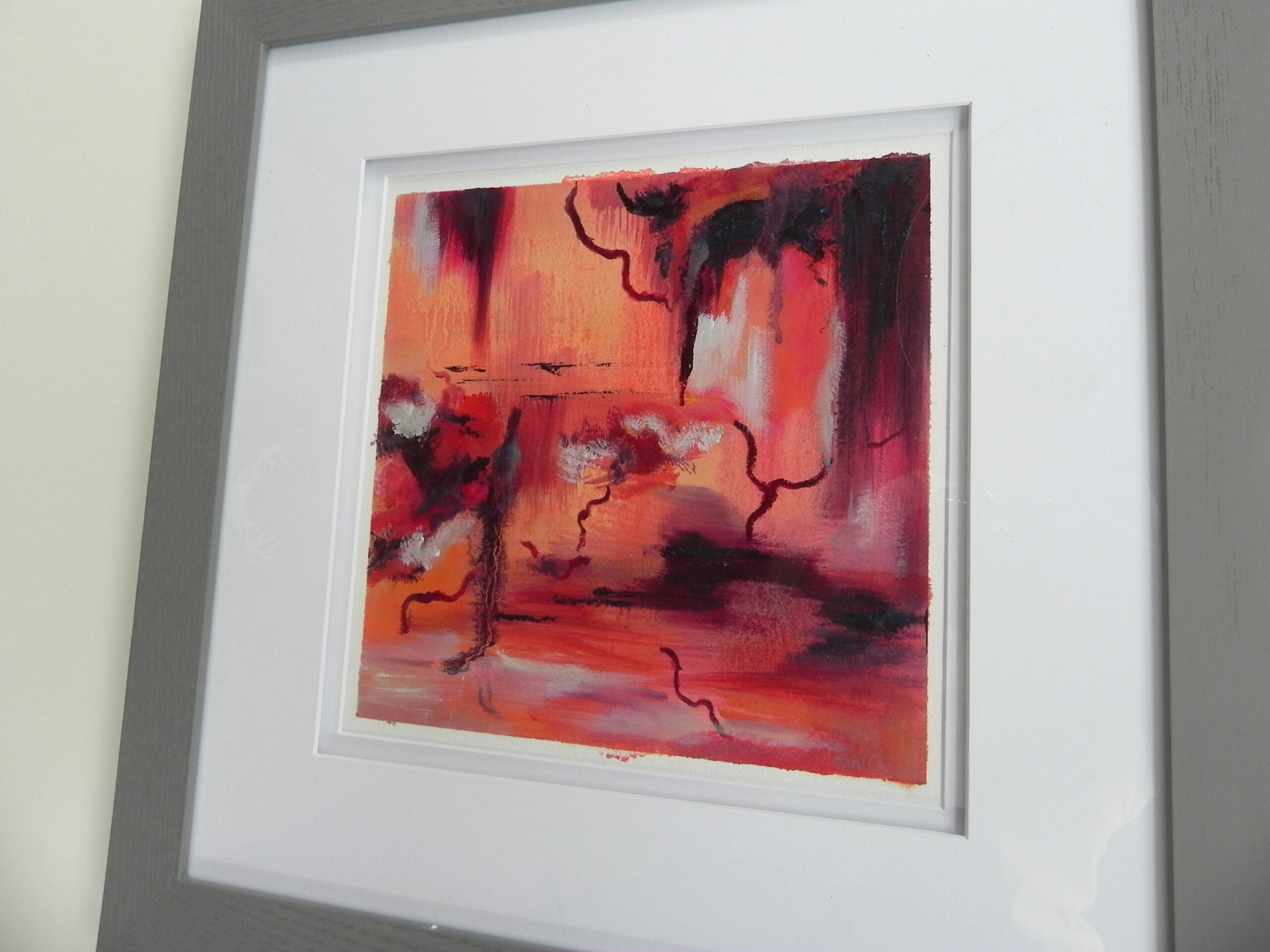 Abstract painting with bold red and orange tones and dark linear accents, presented in a white frame with wide matting