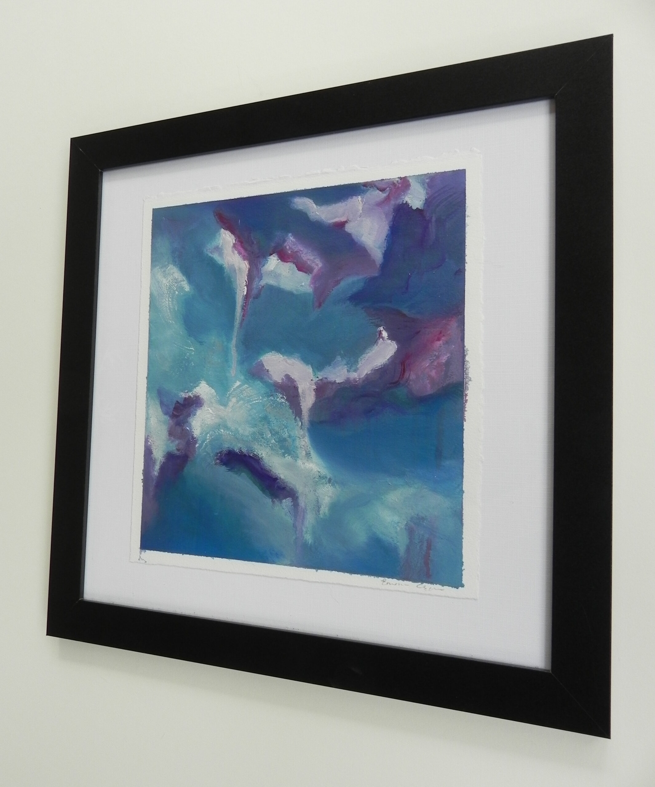 Abstract painting in a black frame with white matting, featuring blue, purple, and white tones against a wall.